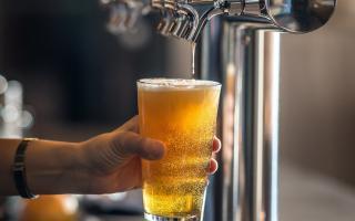 A pint of beer held in a hand inside a pub, showing golden ale and a frothy head.