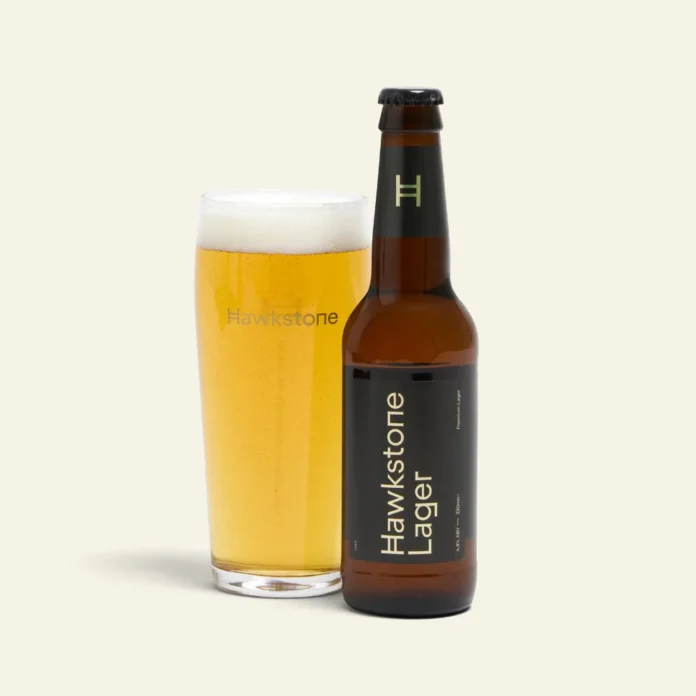 A freshly poured pint of Hawkstone Lager, Jeremy Clarkson’s premium British lager. Pint of Hawkstone Lager with golden colour and foamy head on a wooden pub table.