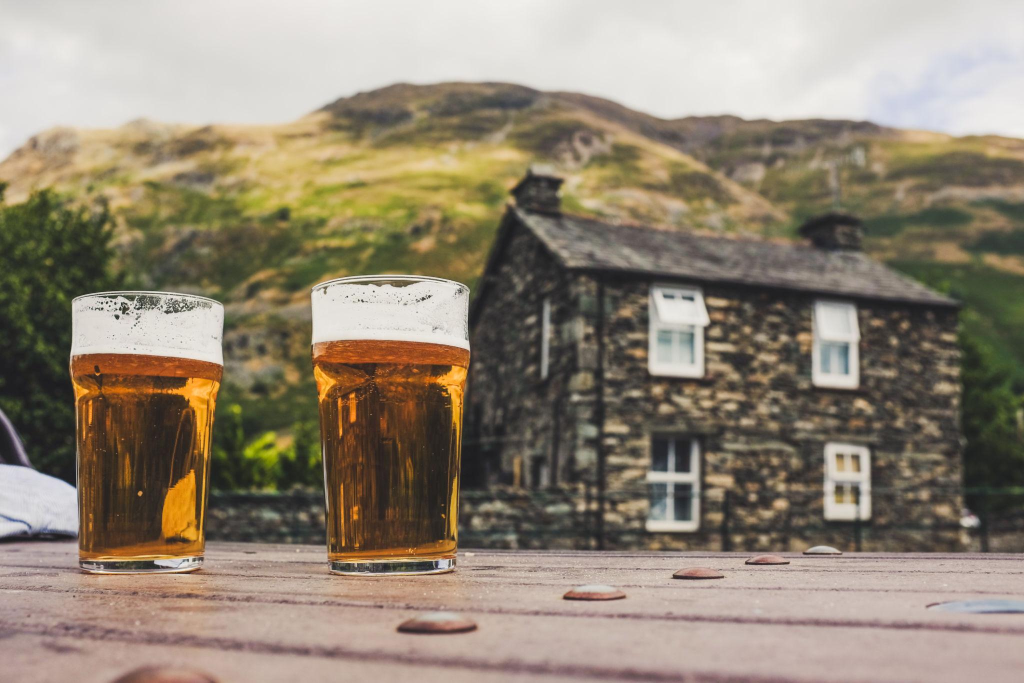 Lake District pubs with pints of beer outside a traditional stone inn in the mountains